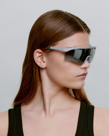 Grå løbe solbriller med mørk glas, set fra siden på dame